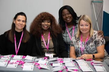 four women sitting behind a desk full of name badges