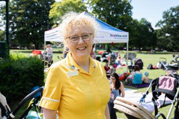 Woman standing in a park at a Healthwatch event, smiling at the camera