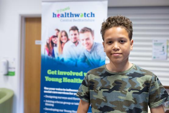 Young boy standing in front of a Healthwatch poster