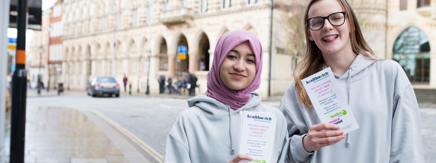 Two young teenagers holding up Healthwatch promotional material