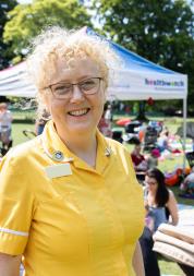 Woman standing in a park at a Healthwatch event, smiling at the camera